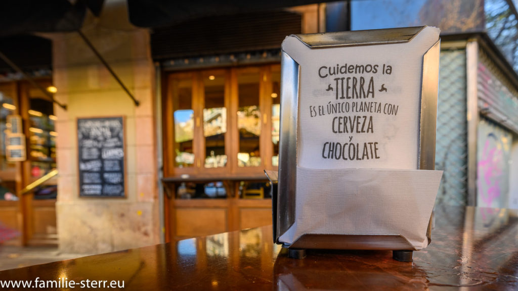 Serviettenbox auf einem Tisch vor einer Tapas - Bar in Barcelona mit dem Aufdruck "Cuidemos la Tierra, es el unico Planeta von Cerveza y Chocolate