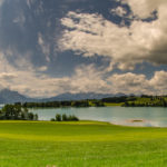 Blick über den Forggensee in die bayerischen Alpen mit weißen Kumuluswolken im weiß-blauen Himmel