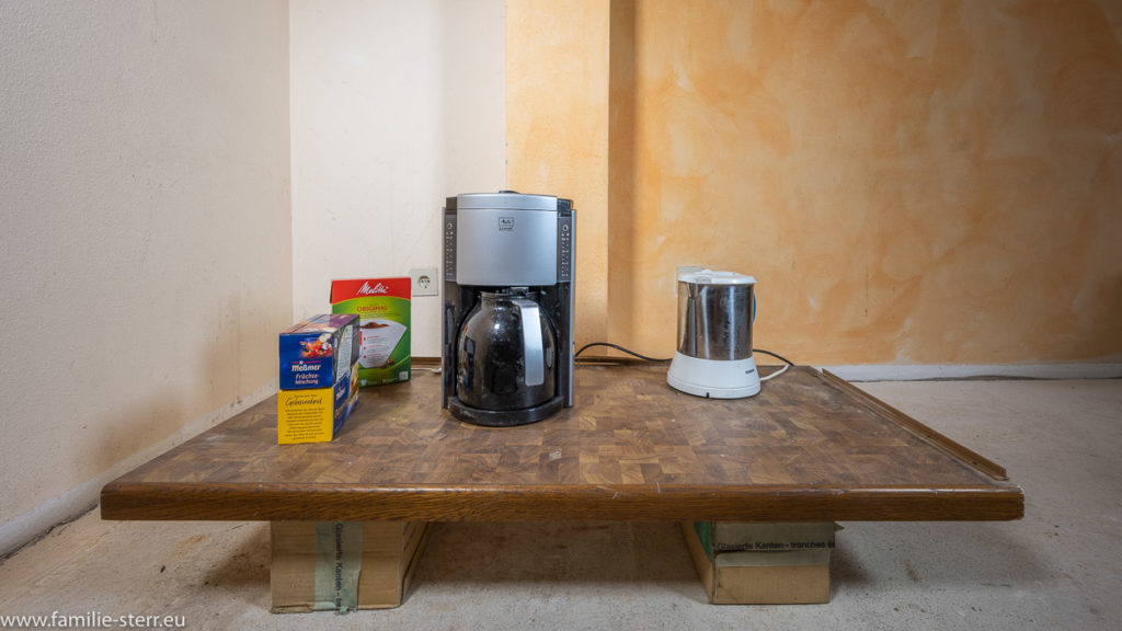 improvisierte Teeküche - ein Holzbrett mit Kaffeemaschine und Wasserkocher auf kleinen Paketen, die als Tischfüße dienen