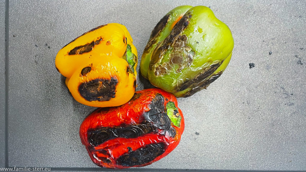 eine rote, eine gelbe und eine grüne Paprika, stark angerollt mit leicht verbrannter Haut