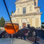 ein Glas Aperol Spritz vor der von der abendlichen Sonne erleuchteten Fassade der Kirche in Castion Veronese