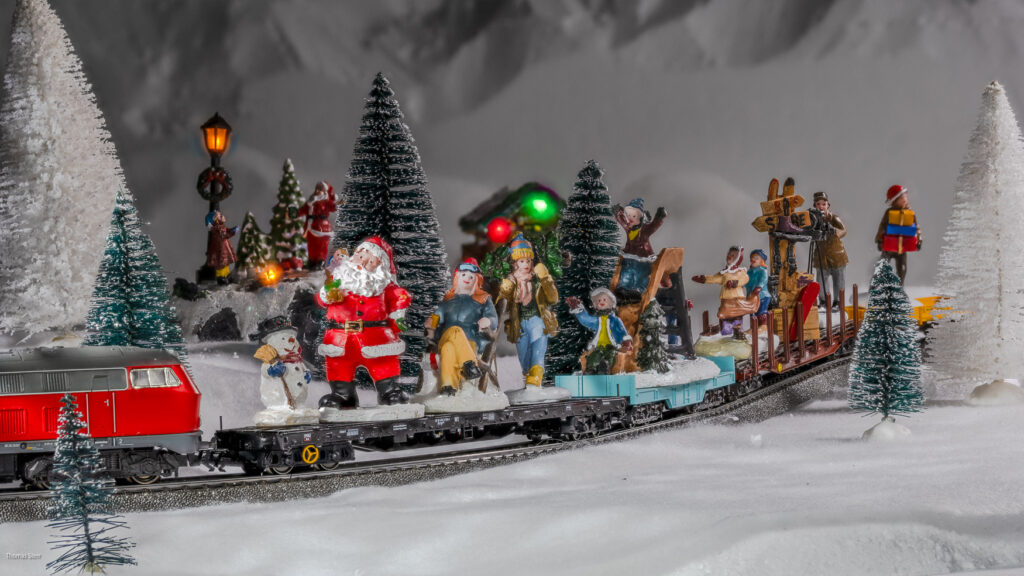 Figuren aus dem Weihnachtsdorf fahren auf dem Zug der Modelleisenbahn am Ende der Weihnachtszeit ins Sommerlager